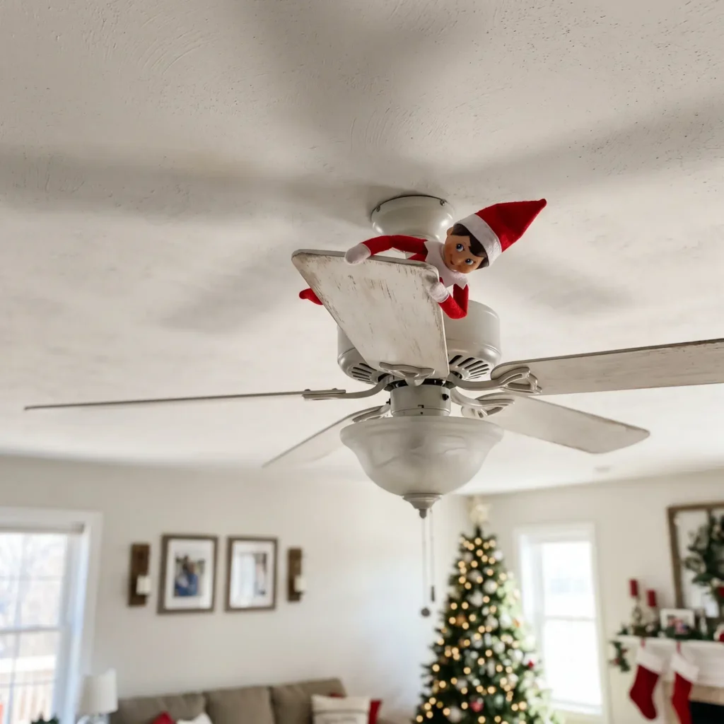 Scout elf looking down from the top blade of a white ceiling fan in a living room.